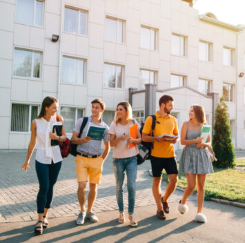 Five friendly students are walking after they passed test outside the college building and discuss the project